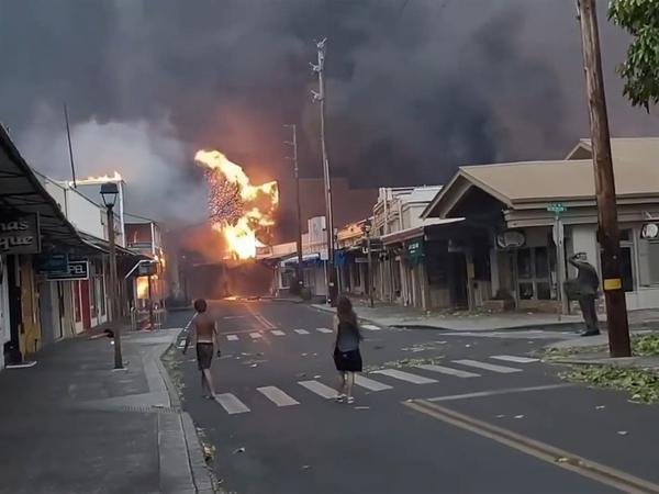 Menschen beobachten Rauch und Flammen eines Waldbrandes. In Hawaii spitzt sich die Lage wegen starker Busch- und Waldbrände auf der Insel Maui zu. F