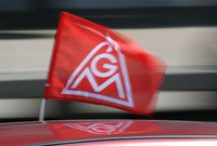 Eine IG-Metall-Flagge spiegelt sich in einem Fahrzeugdach. Die größte deutsche Gewerkschaft ist am stärksten in der Autoindustrie - und hier steht ein tiefer Wandel bevor.