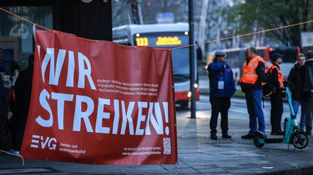 Mitglieder der Bahngewerkschaft EVG stehen in der Nähe des Bahnhofs  Köln an einem Transparent mit der Aufschrift „Wir streiken“. 