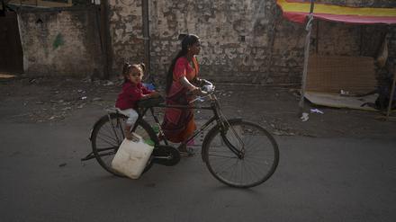 Eine Frau mit einem Kind transportiert Wasser mit einem Fahrrad aus einem öffentlichen Wasserhahn in einem Slumgebiet. In Südasien leiden weltweit am meisten Kinder an Wasserknappheit.