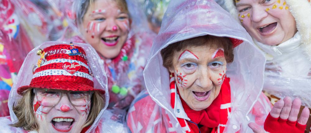 Karnevalisten mit Regenschutz feiern an Weiberfastnacht die Eröffnung des Straßenkarnevals auf dem Alter Markt. 