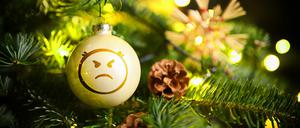 Weihnachtskugel mit Wut-Emoji hängt an einem Weihnachtsbaum, Symbolfoto Streit unterm Weihnachtsbaum, Fotomontage