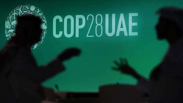 29.11.2023, Vereinigte Arabische Emirate, Dubai: Zwei Menschen unterhalten sich vor einem Logo des UN-Klimagipfels COP28. Bei dem COP28-Treffen wollen mehr als 190 Länder ab Donnerstag am Persischen Golf die erste große Bestandsaufnahme der Umsetzung der Pariser Klimakonferenz 2015 erstellen. Foto: Rafiq Maqbool/AP +++ dpa-Bildfunk +++
