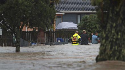 Neuseeland, Auckland: Rettungskräfte und ein Mann waten durch das Hochwasser einer überschwemmter Straße. 