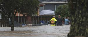 Neuseeland, Auckland: Rettungskräfte und ein Mann waten durch das Hochwasser einer überschwemmter Straße. 