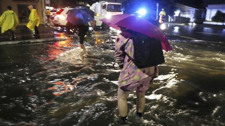Menschen überqueren nach massiven Regenfällen eine überflutete Straße in Auckland, Neuseeland. 