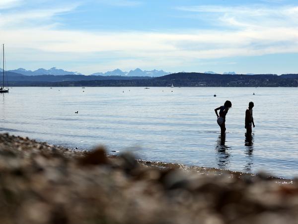 Ein Paar steht am Ufer des Ammersees bei sommerlichen Temperaturen im seichten Wasser. 
