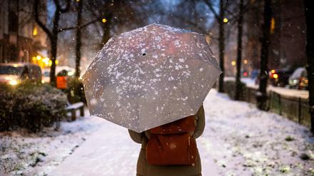 Frau läuft mit einem Regenschirm durch das winterliche Berlin.