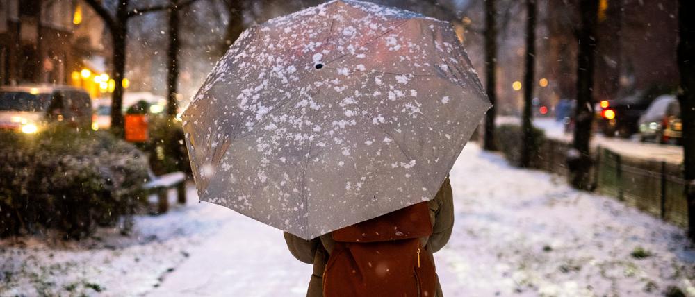 Frau läuft mit einem Regenschirm durch das winterliche Berlin.