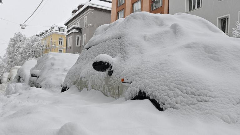 Eine dicke Schneeschicht liegt auf parkenden Autos in München.
