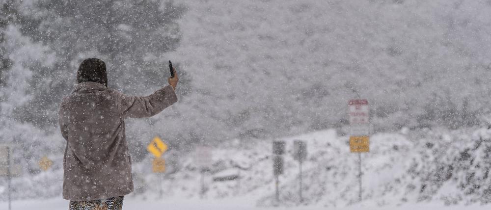 Eine Frau steht auf einer schneebedeckten Straße und macht ein Selfie im Angeles National Forest in der Nähe von La Canada Flintridge. 