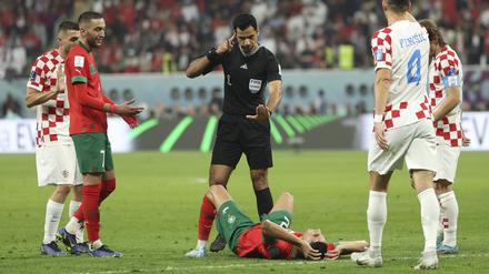 Im Chalifa International Stadion. Schiedsrichter Abdulrahman Al Jassim  gestikuliert, während Achraf Hakimi aus Marokko auf dem Rasen liegt. 