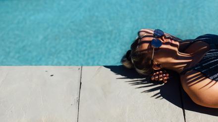 Eine Frau liegt am Rand eines Pools im Schatten.