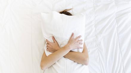Eine Frau liegt rücklings auf dem Bett und umklammert ihr Kopfkissen.