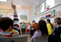 Schülerinnen und Schüler sitzen in einem Klassenraum im Kreis und sprechen mit einer älteren Frau.