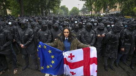 Eine Frau mit einer georgischen Nationalfahne und einer EU-Fahne steht vor Polizisten (Symbolbild).