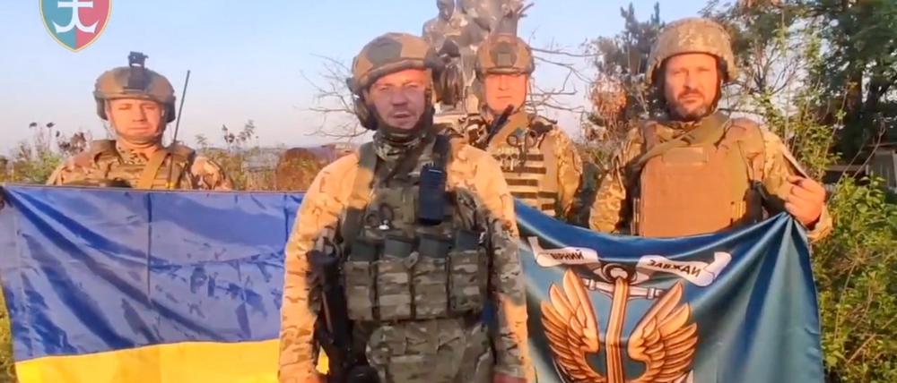 Ukrainische Soldaten stehen mit der ukrainischen Flagge in Uroschajne.