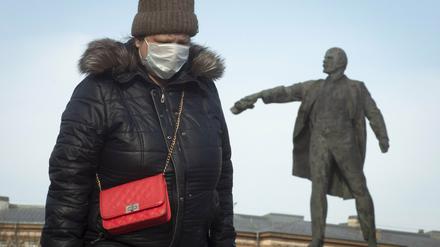 Eine Frau mit Gesichtsmaske geht an einer Statue von Lenin, dem Begründer der Sowjetunion, vorbei.