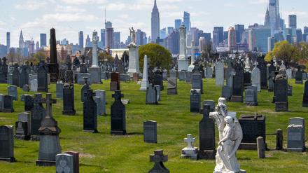 Das Empire State Building und die Skyline von Manhattan hinter den Grabsteinen auf dem Calvary-Friedhof in Queens zu sehen.