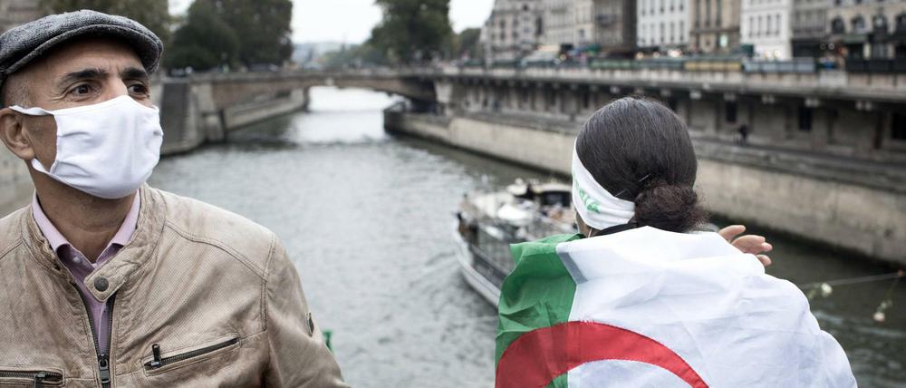 Zwei Personen stehen im Oktober 2020 in Paris an der Seine, eine hat sich die Algerienflagge umgehängt. Sie erinnern an eine Demo im Oktober 1961, bei der mehrere Algerier umgebracht wurden, die gegen den Algerienkrieg demonstrierten.