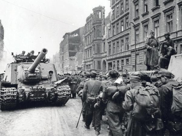 Gefangene deutsche Soldaten in Berlin laufen an einem russischen Panzer und Rotarmisten vorbei. 