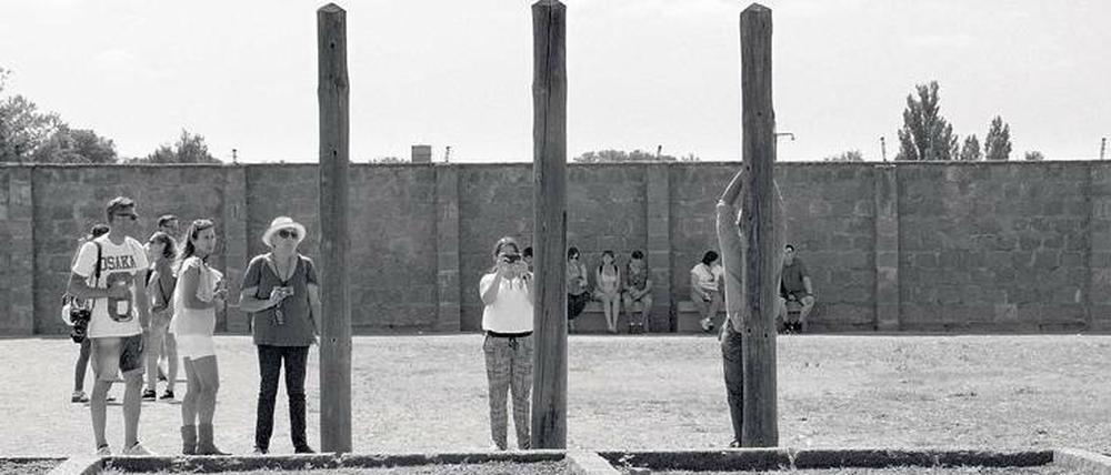 Meditation im Menschenzoo. KZ-Besucher fotografieren sich an Pfählen, wo Häftlinge damals die Arme gebrochen wurden.
