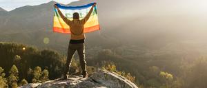 Der Mensch und die Natur. Ein Wanderer hält eine LGBTQ-Flagge hoch.
