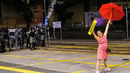 Eine Demonstrantin streckt einen Regenschirm und ein Schild in die Höhe, während Polizisten mit Tränengas auf sie zielen.