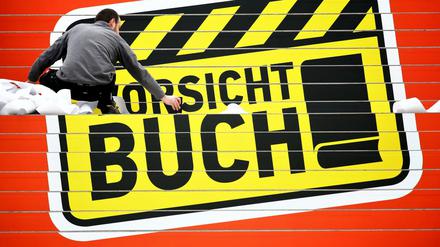 Ein Werbetechniker klebt das Logo "Vorsicht Buch!" der Leipziger Buchmesse auf eine Treppe in der Glashalle der Leipziger Messe. 