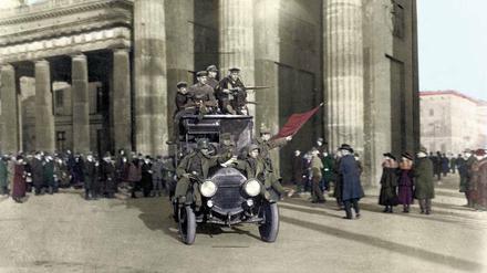 Ganz ohne Bahnsteigkarte. Revolutionäre Truppen bahnen sich am 11. November 1918 vor dem Brandenburger Tor ihren Weg durch überraschte, doch nach guter Sitte ausgehfein gekleidete Bürger (zeitgenössisch handkolorierte Aufnahme).