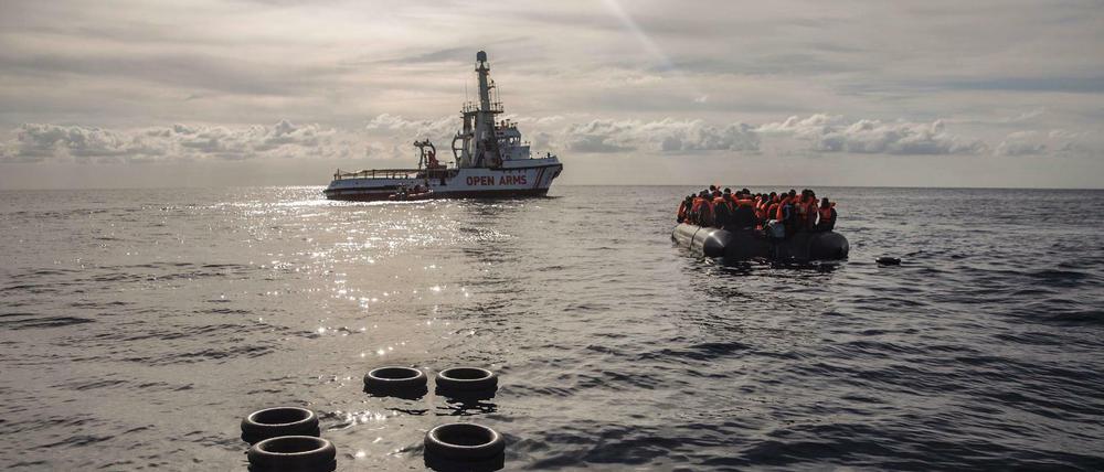 Migranten in einem Schlauchboot und ein Boot der NGO Proactiva Open Arms im zentralen Mittelmeer.