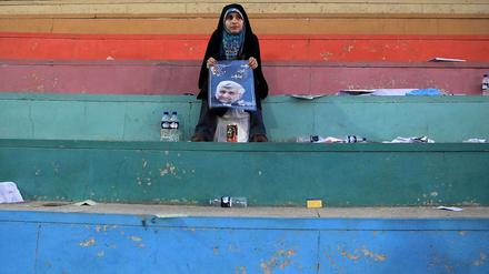 Nach einer Wahlkampfveranstaltung sitzt eine schwarz verschleierte Frau auf einer Treppe und zeigt ein Plakat des Präsidentschaftskandidaten Jalili.