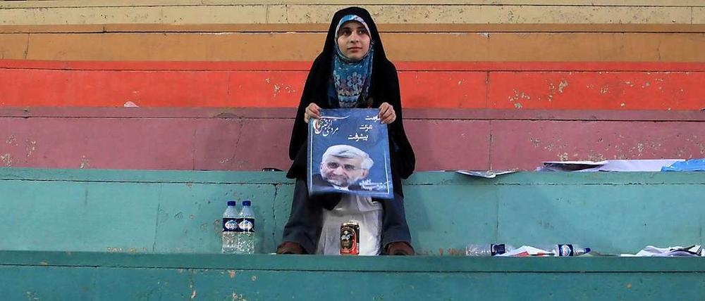 Nach einer Wahlkampfveranstaltung sitzt eine schwarz verschleierte Frau auf einer Treppe und zeigt ein Plakat des Präsidentschaftskandidaten Jalili.