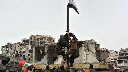 In der zerstörten Stadt Homs hissen Soldaten die syrische Fahne, nachdem die Rebellen abgezogen sind. 