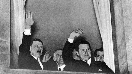 Der neu ernannte Reichskanzler Adolf Hitler grüßt nach der Machtübernahme am 30. Januar 1933 aus einem Fenster in Berlin heraus den vorbeiziehenden Fackelzug. Neben ihm stehen Innenminister Wilhelm Frick, Reichsminister Hermann Göring und der spätere Stellvertreter Hitlers, Rudolf Heß.