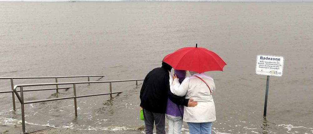Eine Familie steht auf einem Deich an der Nordsee in Dornumersiel unter einem roten Schirm im Regen und blickt auf das Wasser.