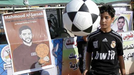 Ein palästinensischer Junge spielt Fußball neben einem Plakat, das Mahmoud Sarsak zeigt. In Palästina wird regelmäßig für die Freilassung des ehemaligen Nationalspielers demonstriert. Nun, da Europa im Fußballfieber ist, findet sein Fall auch international Beachtung.