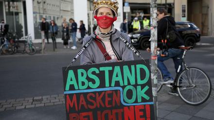 Eine Demonstrantin mit selbst gebautem Mundschutz und einer Plastikkrone steht am Rande einer Demonstration am Rosa-Luxemburg-Platz. 