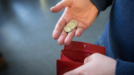 Münzen im Wert von fünf Euro liegen in einer Hand über einem Portemonnaie. 