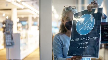 Eine Frau entfernt ein 2G Hinweisschild an einem Geschäft in Kiel. (Archivbild)