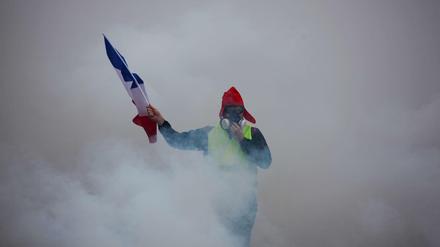 Ein Demonstrant mit französischer Flagge und gelber Weste demonstriert inmitten von Tränengas. 