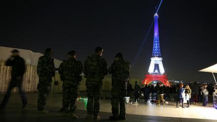 Zum Gedenken leuchtet der Eiffelturm am Montagabend in Bleu-blanc-rouge, davor patrouillieren Soldaten zur Terrorabwehr.