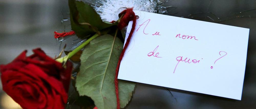 Eine Rose, durch ein Einschussloch einer Scheibe gesteckt in Paris. Auf dem Zettel steht: "Im Namen von was?"