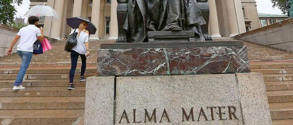 Vor den Treppen zu einem Gebäude steht eine Statue mit der Aufschrift "Alma Mater"