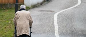 Eine ältere Frau geht mit einem Rollator auf einem Weg entlang.