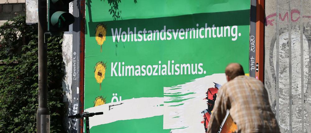 Ein beschädigtes Plakat mit den Schriftzügen "Wohlstandsvernichtung" und "Klimasozialismus" hängt am Straßenrand.