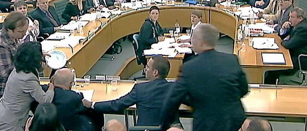 Angriff von links. Rupert Murdoch wird von einem Mann (links im Bild) während der Anhörung im Parlament attackiert.