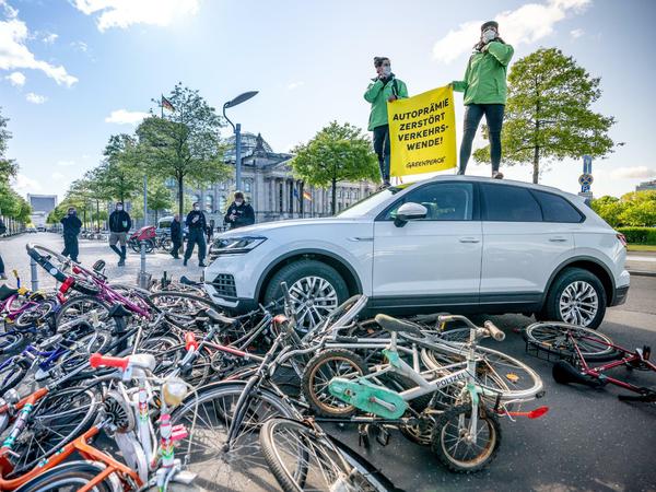 Aktivisten von Greenpeace demonstrieren vor dem Reichstag mit einer Aktion, bei der ein Auto über Fahrräder fährt.