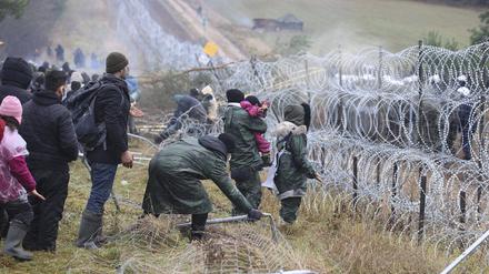 dpatopbilder - 08.11.2021, Belarus, Grodno: Migranten stoßen an der weißrussisch-polnischen Grenze einen Zaun um, während die Polizei hinter einem Stacheldrahtzaun steht. Mehrere Hundert Migranten haben sich nach Angaben der Behörden in Belarus zu Fuß auf den Weg zur Grenze zum EU-Nachbarland Polen gemacht. Foto: Leonid Shcheglov/BelTA/AP/dpa +++ dpa-Bildfunk +++