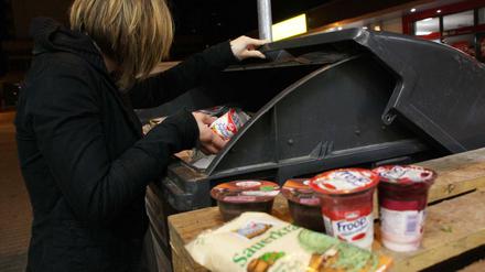 Eine Jugendliche in Berlin sucht nachts in einer Abfalltonne nach verwertbaren Lebensmitteln.